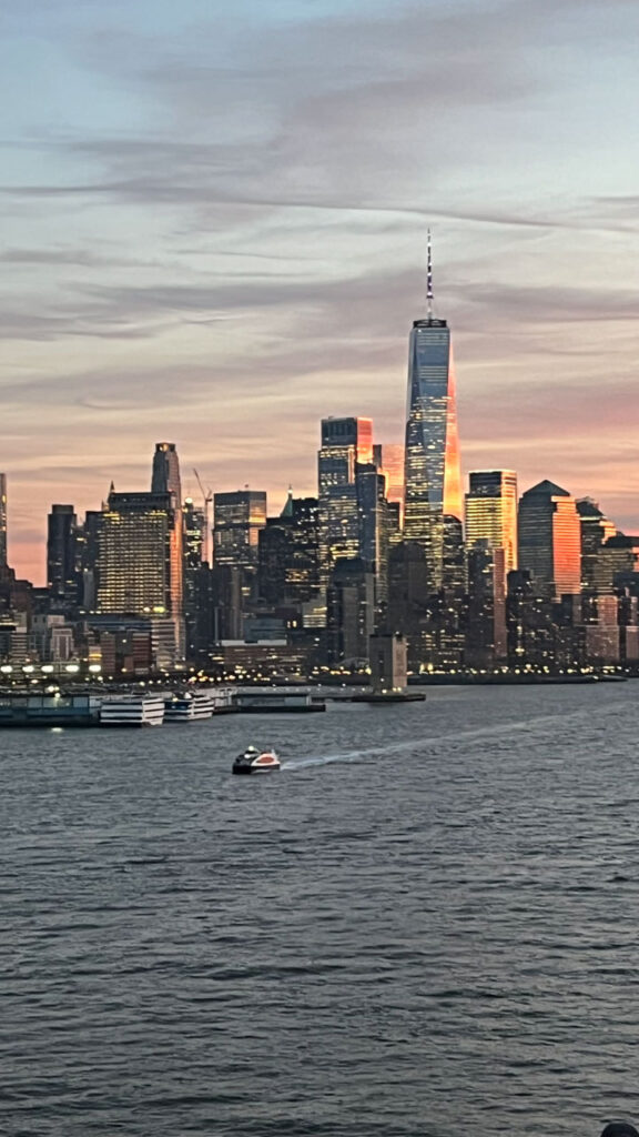 Sailing out of Manhattan, New York City, NY on the Carnival Venezia with sunset reflecting in One World Trade Center and other New York City buildings