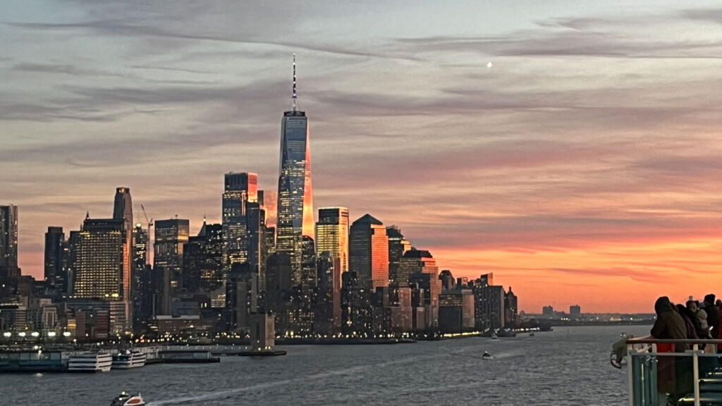 Sailing out of Manhattan, New York City, NY on the Carnival Venezia with sunset reflecting in One World Trade Center and other New York City buildings