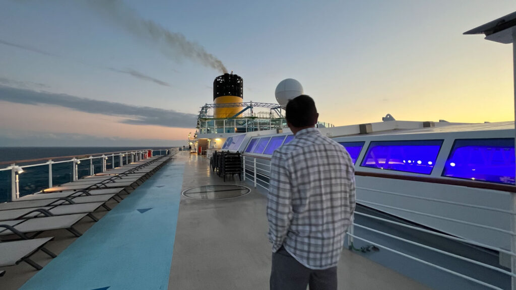 Walking around deck twelve next to the magradome (sliding covered roof over decks ten and eleven midship) on the Carnival Venezia. Part of the jogging track is on the left and the ropes course, the miniature golf course and the Warehouse arcade are ahead near the smokestack.